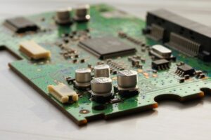 This image displays a green printed circuit board (PCB) adorned with various electronic components like capacitors and chips. Amidst the intricate circuitry, we want to let you know that "We’re Open for Business! Need PCB Layout & Design Services We've Got You Covered", ready to craft and shape PCBs to meet your specific requirements.